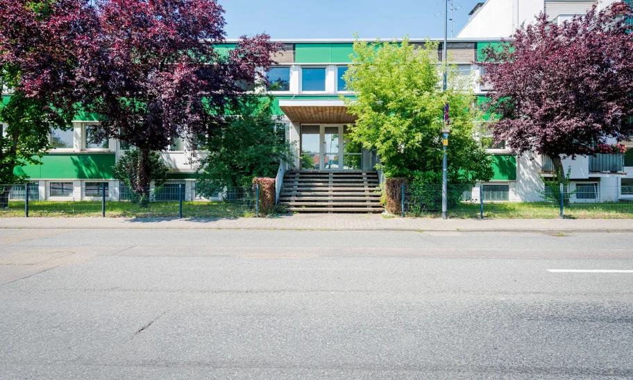 Bürogebäude mit grüner Fassade hinter blühenden Bäumen an der Straße