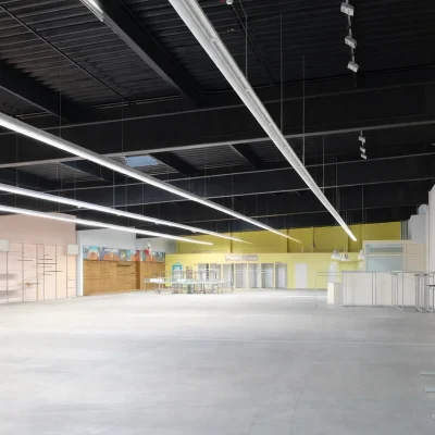 Leere Gewerbehalle mit bunten Wandflächen in Rosa und Gelb sowie leeren Regalsystemen