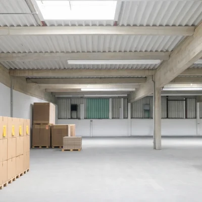 Lagerhalle mit Kartonstapeln, Oberlicht und grüner Trennwand im Hintergrund