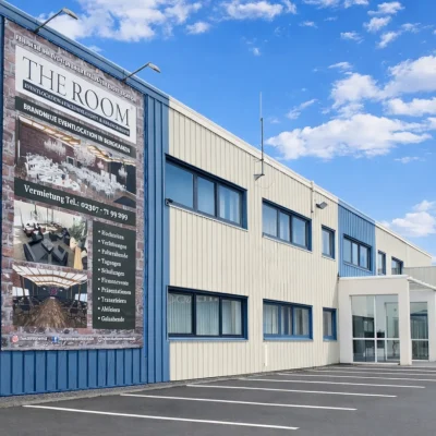Gewerbegebäude mit Eventlocation-Werbeplakat und leerem Parkplatz davor