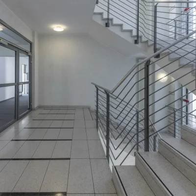 Treppenhaus mit Fliesenboden, Metallgeländer und Glaseingangstür