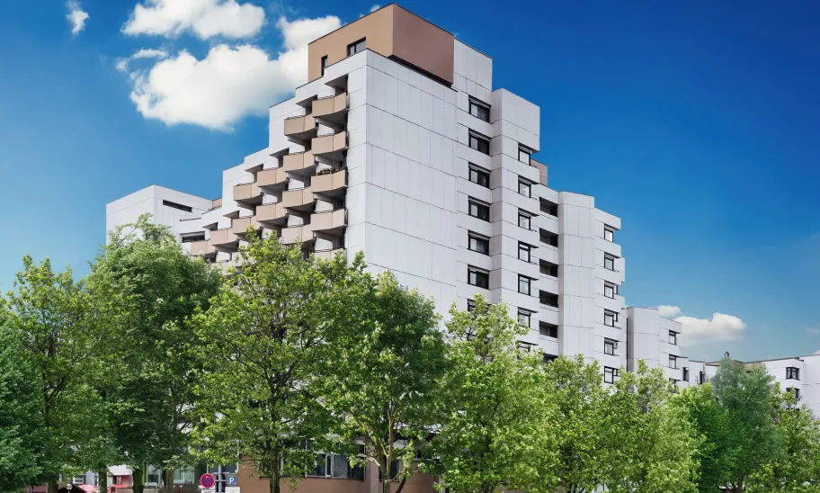 Terrassenartig gestaffeltes Bürogebäude mit heller Fassade und Balkonen hinter Straßenbäumen und Parkplatz