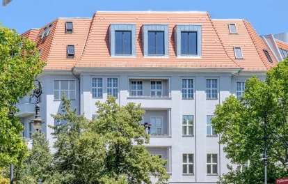 Berliner Altbau mit rotem Ziegeldach, Zinkgauben und Straßenbäumen vor blauem Himmel