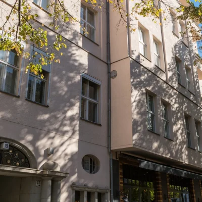 Altbau-Eingang mit Rundbogen und Säulen, Fassade im Baumschatten und Gastronomie im Erdgeschoss