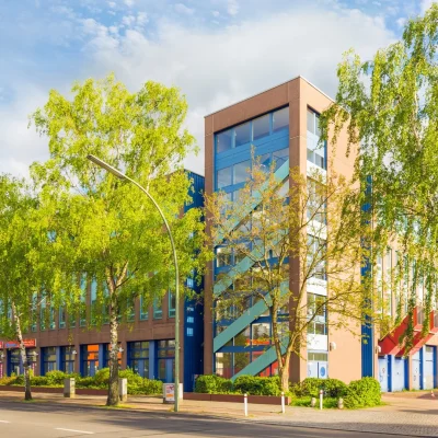 Bürogebäude mit blauem Treppenturm, Birken im Vordergrund und langgestrecktem Gebäuderiegel an der Straße