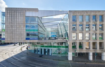 Geschäftshaus mit Fassade aus hellem Naturstein und Glas, Ladenzone im Erdgeschoss an einer Straßenbahnkreuzung