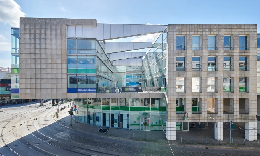 Geschäftshaus mit Fassade aus hellem Naturstein und Glas, Ladenzone im Erdgeschoss an einer Straßenbahnkreuzung