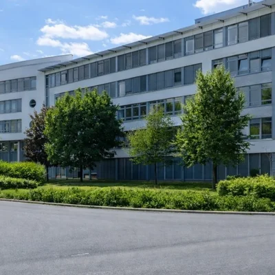 Mehrgeschossiger Bürobau mit Bandfenstern, Bäumen und Grünstreifen an einer Straße (KI-Visualisierung)