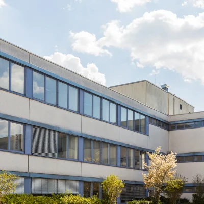 Fassade des Bürogebäudes DO3 mit blau gerahmten Bandfenstern, Jalousien und blühenden Bäumen im Innenhof