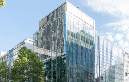 Eckgebäude mit Glasfassade und Staffelgeschoss an einer Straßenkreuzung in Frankfurt mit Straßenbäumen