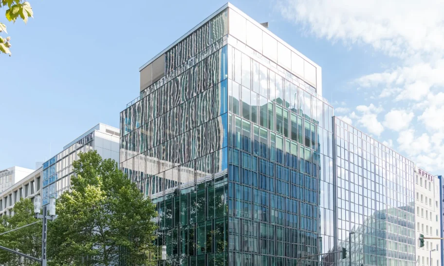 Eckgebäude mit Glasfassade und Staffelgeschoss an einer Straßenkreuzung in Frankfurt mit Straßenbäumen
