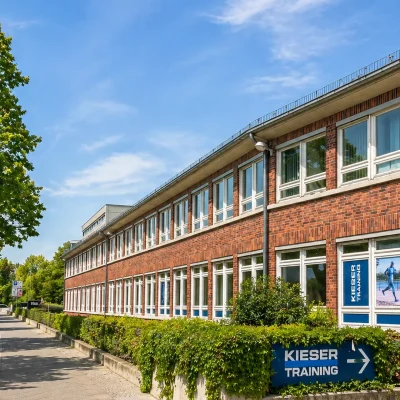 Langgestrecktes Backsteingebäude im Gewerbepark Schmargendorf mit weißen Fenstern an einer baumgesäumten Straße