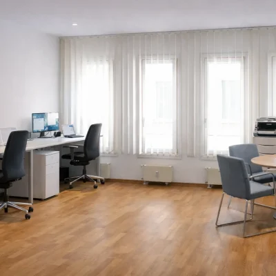 Büroraum mit Schreibtischen, Besprechungstisch, Flipchart und Pinnwand bei Tageslicht
