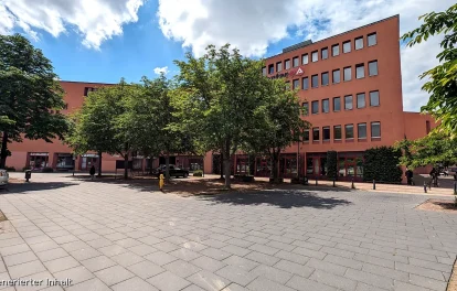 Jobcenter-Gebäude hinter grünen Bäumen auf sommerlichem Vorplatz