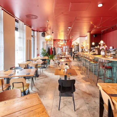 Restaurant mit roter Decke, Holztischen, grüner Bar und Flaschenregal im Hintergrund