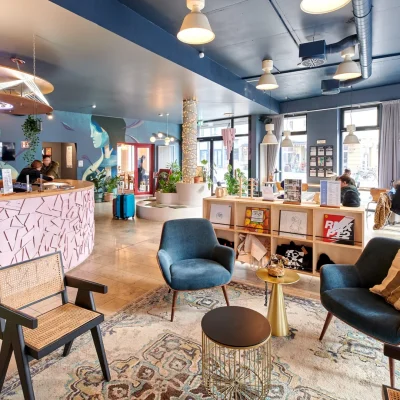 Helle Hotellobby mit rosa Rezeption, blauen Samtsesseln, Schallplattenregal und großem Wandbild