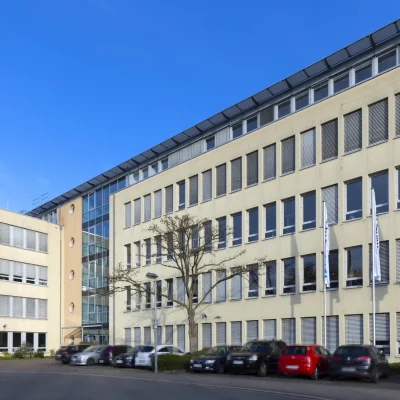 Frontansicht des Bürogebäudes mit Parkplatz und Firmenschild auf dem Dach