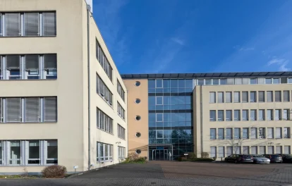 Gebäudeeingang mit Glasfront, Rundfenstern und angrenzendem Parkplatz