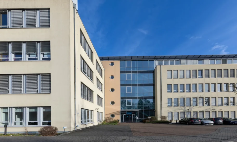 Gebäudeeingang mit Glasfront, Rundfenstern und angrenzendem Parkplatz