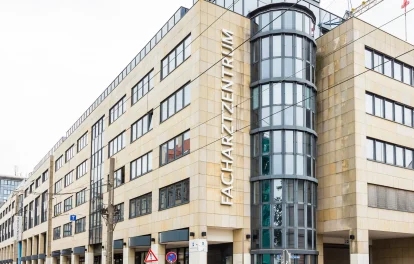Fassade des Facharztzentrums mit rundem Glasturm und Baukran im Hintergrund