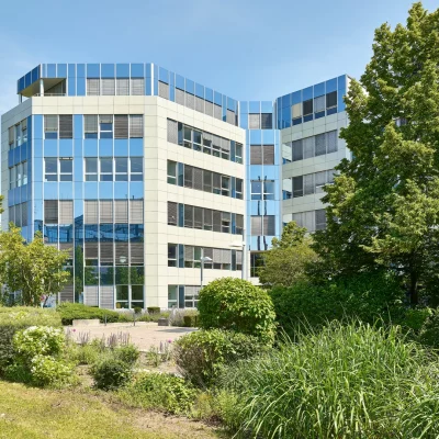 Bürogebäude mit Glasfassade, Bäumen und gepflastertem Weg