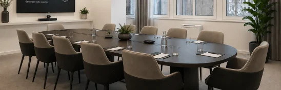 Besprechungsraum mit ovalem dunklem Tisch, gepolsterten Stühlen, Bildschirm und Fensterfront (KI-Visualisierung)