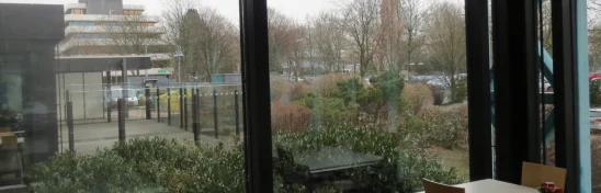 Innenansicht eines Aufenthaltsbereichs im Bürogebäude Adickesallee in Frankfurt mit großen Fensterfronten und Blick ins Grüne sowie angrenzende Außenflächen.