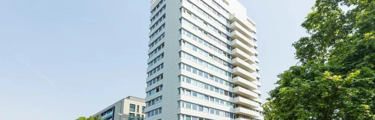 Straßenansicht eines modernen Bürohochhauses in der Adickesallee in Frankfurt mit direkter Anbindung an den öffentlichen Nahverkehr und umgebender städtischer Bebauung.